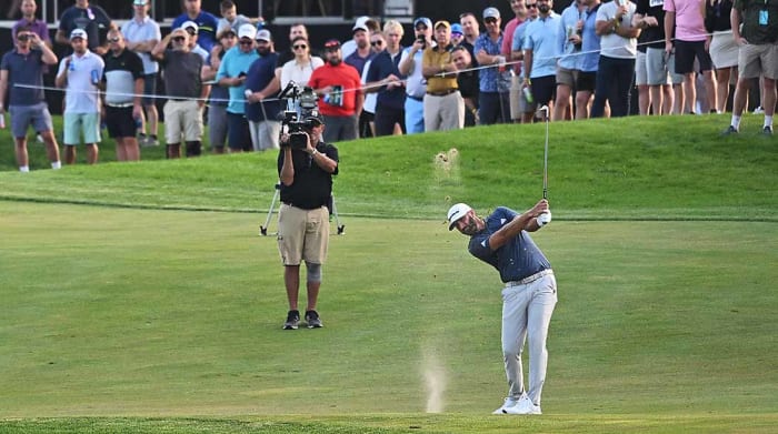 Dustin Johnson is pictured hitting a shot in front of a TV camera at the 2022 LIV Golf Invitational Chicago.